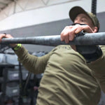 Person performing pull-ups with bear komplex hand grips on a bar in an indoor setting