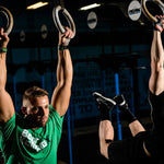 Two men exercising with rings in a gym setting, with bear complex gymnastic grips