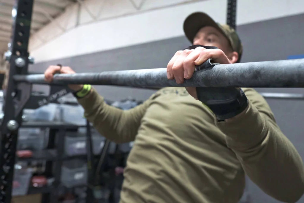 Person performing pull-ups with bear komplex hand grips on a bar in an indoor setting