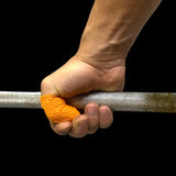 Hand holding a barbell with orange frog grip thumb tape on a black background