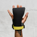 Black wrist support with yellow strap on a person's wrist against a plain background