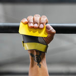 Hand wearing a black and yellow hand grip holding onto a barbell.