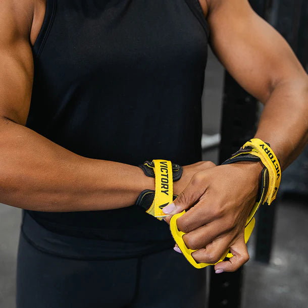 Person wearing black athletic wear with yellow victory hand grips on a blurred background