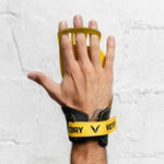 Hand wearing a black wrist wrap with a yellow logo against a white brick wall.