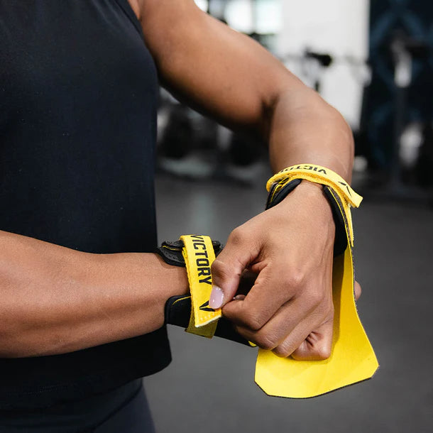 Person wrapping a wrist with yellow wrist wrap labeled 'Victory' in a gym setting