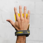 Hand wearing a gray hand grip with yellow accents on a plain background