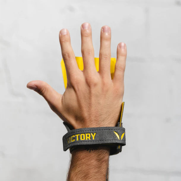 Hand wearing a gray hand grip with yellow accents on a plain background