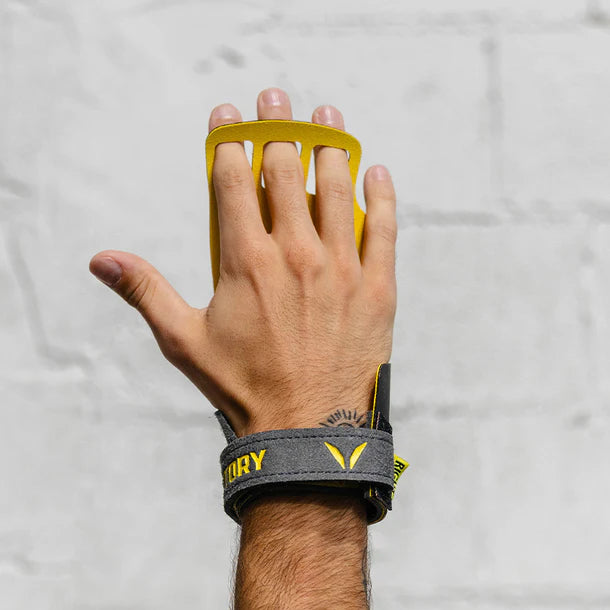 Hand wearing a yellow and gray Victory wrist hand grips on a light gray background