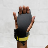 Hand wearing a black victory hand grip with yellow wrist strap on a white background
