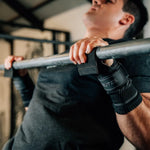 CrossFit athlete gripping a pull-up bar wearing black Velites All Terrain gymnastic grips