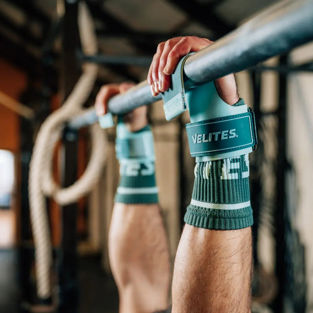 Athlete gripping a bar wearing mint Velites All Terrain gymnastic grips in a CrossFit gym