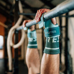 Athlete gripping a bar wearing mint Velites All Terrain gymnastic grips in a CrossFit gym
