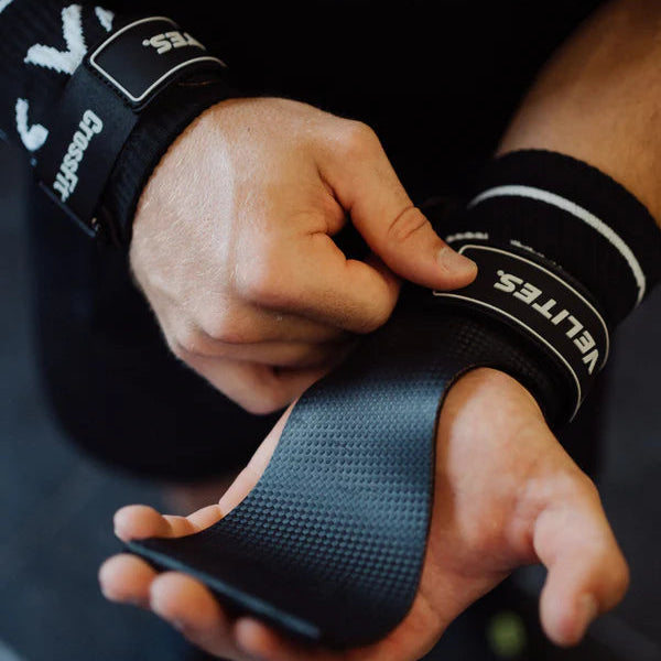 CrossFit athlete putting on black Velites Quad Ultra no chalk gymnastic grips showing textured grip surface and CrossFit branding