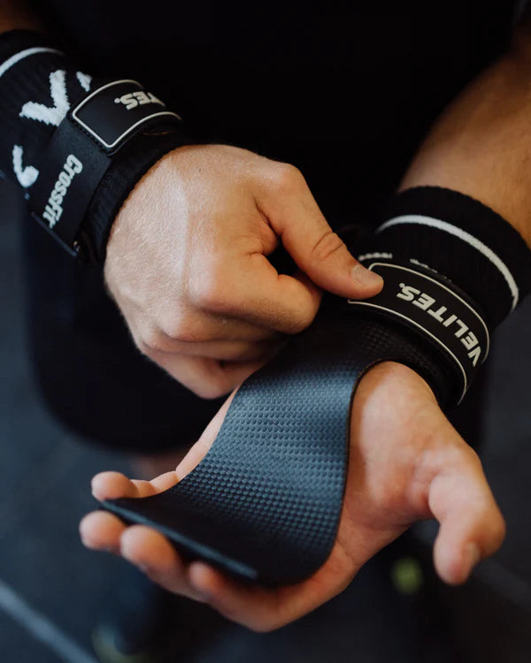 CrossFit athlete putting on black Velites Quad Ultra no chalk gymnastic grips showing textured grip surface and CrossFit branding