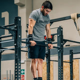 Male CrossFit athlete performing bar muscle-ups wearing black Velites Quad Ultra no chalk gymnastic grips in CrossFit box
